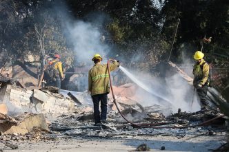 A crew hoses down the smoldering remains of a building in Altadena.