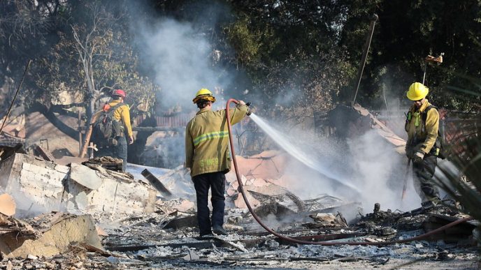 A crew hoses down the smoldering remains of a building in Altadena.