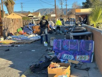 A San Bernardino police officer and city workers remove an encampment Jan. 8 in an alley near Baseline Street.